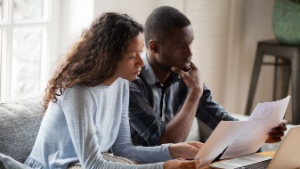 worried couple sitting on sofa looking at paperwork